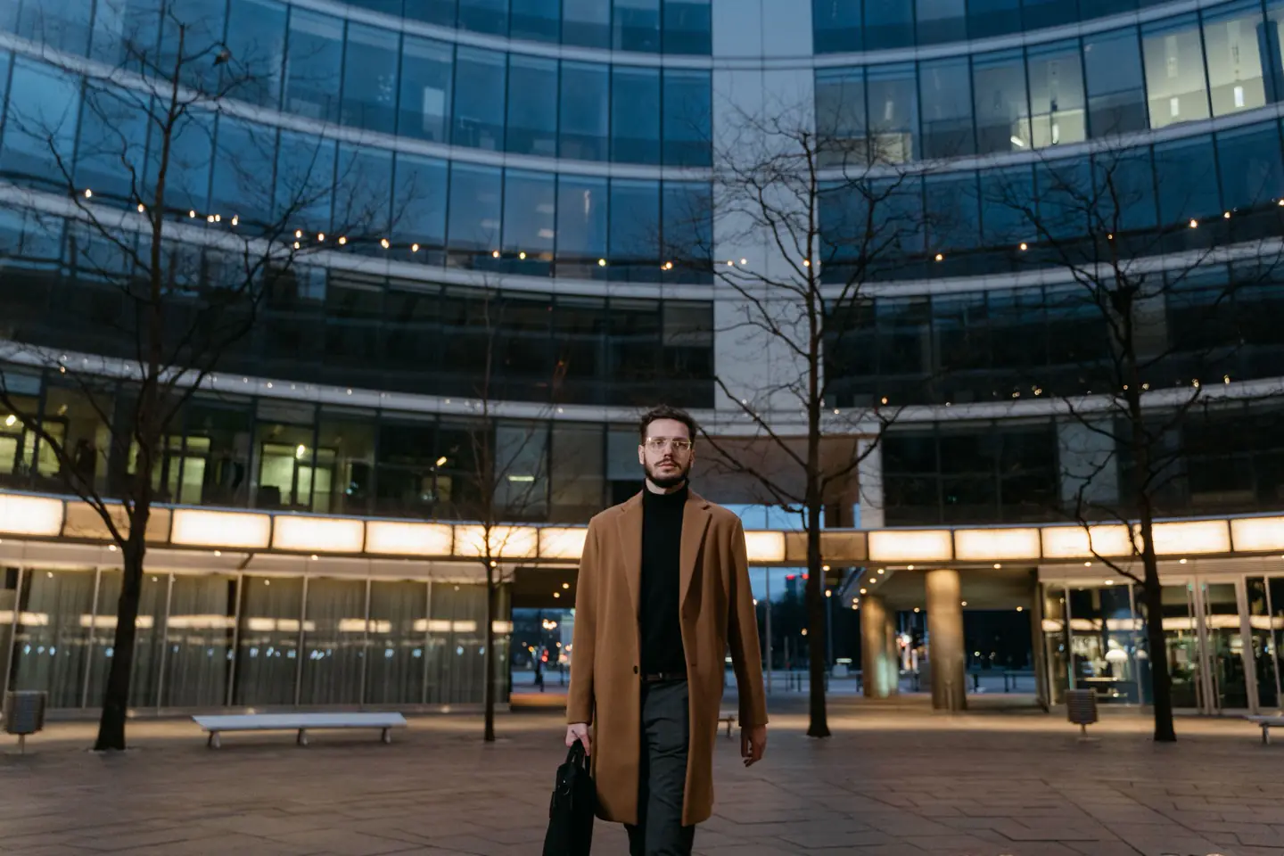 Person mit Laptoptasche am Abend vor einem beleuchteten Bürogebäude